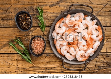 Frozen cooked shrimp with rosemary in rustic pan on wooden table. Icy seafood ingredient with copy space, top view