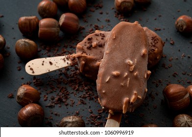 Frozen dessert and summer snack concept with close up on two delicious chocolate and hazelnut ice cream bars surrounded by scattered hazelnuts, cocoa powder and shaved chocolate on dark background - Powered by Shutterstock