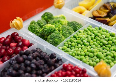 Frozen Fruits And Vegetables. Products Are Poured Into Plastic Boxes. In The Center Of The Frame Is Broccoli And Green Peas. Freezer Shop Window.