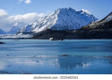 A frozen glacial lake with icebergs floating in the shadow of snow-covered mountains in New Zealand. The landscape presents a breathtaking winter scene filled with icy reflections. - Powered by Shutterstock