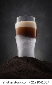 Frozen glass of beer with dark stout beer on a black sand and dark background. Selective focus