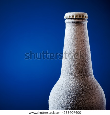 Frozen glass bottle of beer on blue. 
