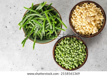 Frozen green beans, frozen peas, frozen white corn close up in a bowl on light grey background, flat lay, copy space
