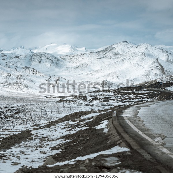 A frozen highway leading to snow-covered\
beautiful mountains in\
daylight