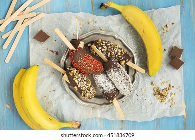 Frozen Homemade Banana Pops Covered With Chocolate, Sprinkles, Nuts And Coconut Chips. Top View