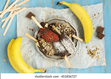 Frozen Homemade Banana Pops Covered With Chocolate, Sprinkles, Nuts And Coconut Chips. Top View