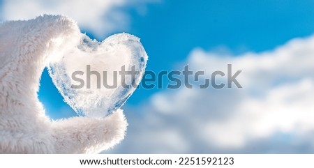 frozen icy heart hand, winter background against clear blue sky and clouds, concept love, romantic, February 14, Valentine's day. festive winter season. Christmas New Year holiday. approach of spring