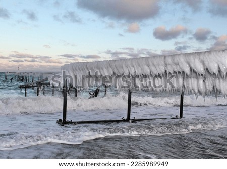 Frozen jetty in the sea with many Big  white icicles on a frosty day with blue sky and Grey cloudes