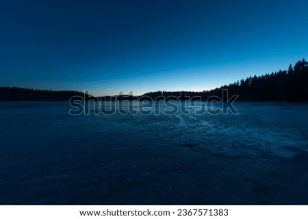 Frozen lake ice in the blue light after the sunset in the forests of Pirkanmaa, Finland