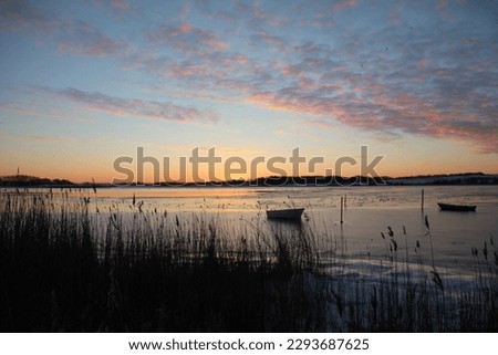 Frozen lake with small boats on thick uneven surface of thick layer of ice on a Beautiful evening with colours from the sunset
