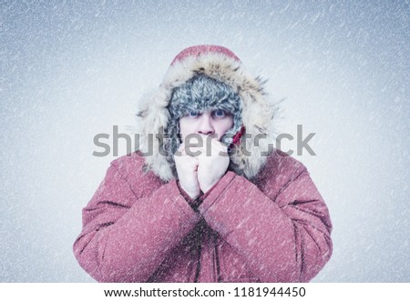 Frozen man in red winter clothes warming hands, cold, snow, frost, blizzard