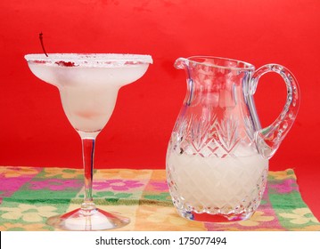 Frozen Margarita In Long-stem Glass With Crystal Pitcher Containing More Margarita To One Side.  Colorful Hispanic Setting With Copy Space.