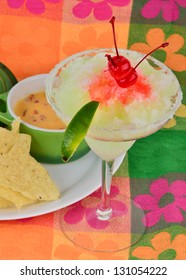 Frozen Margarita With Maraschino Cherry And Lime On Brightly Colored Background Served With Chili Con Queso Dip And Tortilla Chips.