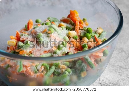 Frozen mixed vegetables, including carrots, beans, peas and sweet corn, defrosting in a glass bowl.  On a concrete background