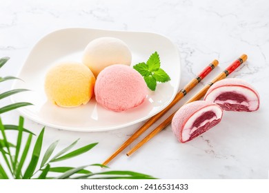 Frozen Mochi lies on a white plate with mint leaves. Nearby, on a marble background, is cut mochi with filling. Bamboo sticks. Perfect retouching. Advertising. Side view. Photo - Powered by Shutterstock