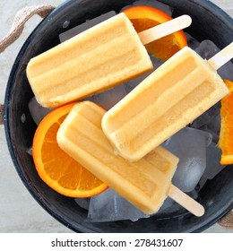Frozen orange yogurt popsicles close up in an rustic ice filled tin pail with fresh fruit slices
