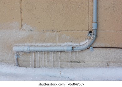 Frozen Pipes Downspout On Snowy Icy Ground Alley Block Wall