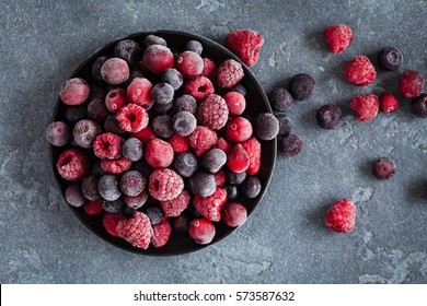 Frozen raspberry, blueberry, cranberry on black background. Frozen fruit. Top view, flat lay, close up.