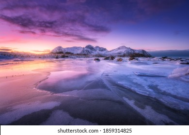 Frozen Sea Coast At Colorful Sunset In Lofoten Islands, Norway. Snowy Mountains, Sea With Frosty Shore, Ice, Reflection In Water, Purple Sky . Winter Landscape With Snow Covered Rocks, Fjord At Night