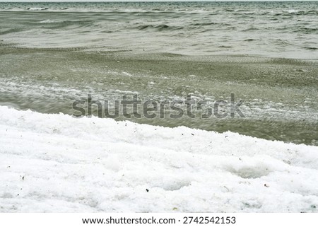 Frozen snow in the foreground, a thin layer of ice at the shoreline and moving sea beyond: three states of water meet beneath a cool winter sky.