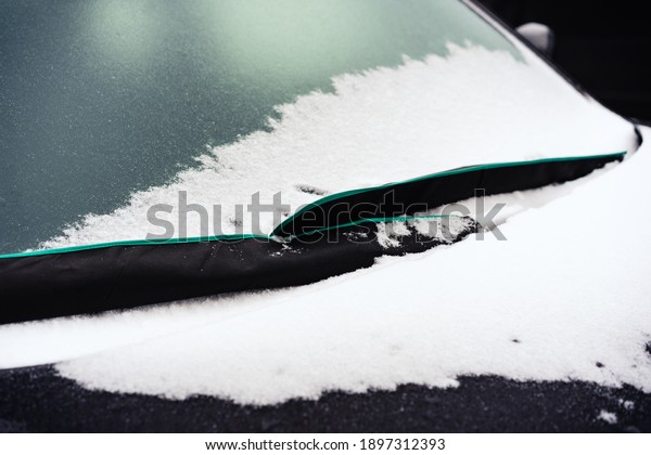 Frozen snowy car\
windscreen in winter, when temperatures drop below zero. Windshield\
wipers in protective\
covers.