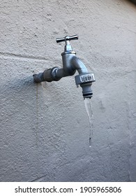 A Frozen Water Faucet On A Concrete Wall With Icicle That Drops