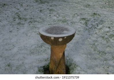 Frozen Water in a Stone Bird Bath Surrounded by Snow in a Country Cottage Garden in Rural Devon, England, UK