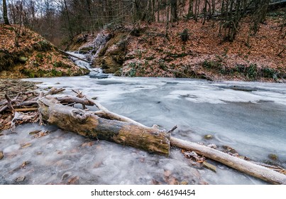 숲 속의 강에 있는 얼어붙은 폭포. 땅의 오래된 갈색 잎 스톡 사진