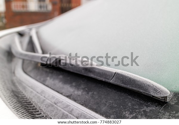 Frozen windscreen and wiper blades on a\
car parked in a street in below zero\
temperatures