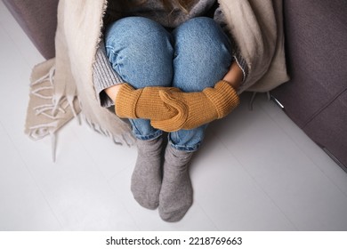 Frozen. A Young Woman Sits On The Floor In An Apartment In A Warm Sweater, Plaid And Mittens And Is Shivering From The Cold. 