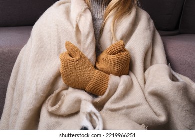 Frozen. A Young Woman Sits On The Floor In An Apartment In A Warm Sweater, Plaid And Mittens And Is Shivering From The Cold. 