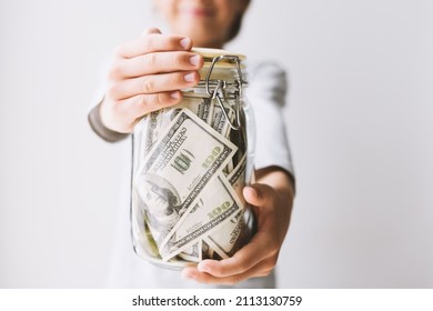 Frugal caucasian teenager boy holding glass jar piggy bank with money dollars in hands. Kid save money Saving money for education learning hobby in future Teaching child financial literacy - Shutterstock ID 2113130759