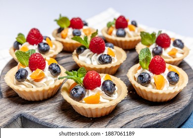 Fruit and berry tartlets dessert assorted on wooden tray. Closeup of delicious pastry sweets pies colorful cakes with fresh natural raspberry blueberry and cheese cream. French bakery catering - Powered by Shutterstock