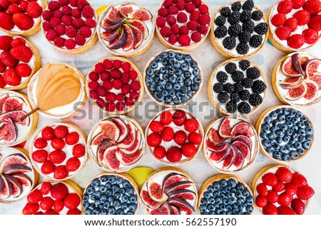 Fruit and berry tartlets dessert tray assorted top view background. Beautiful delicious tarts, bright, colorful pastry cakes sweets with fresh raspberries, figs, strawberry. French Bakery pattern.