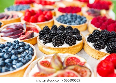 Fruit and berry tarts dessert tray assorted. Closeup of beautiful delicious pastry sweets with fresh natural blackberries and figs. French Bakery catering. Filtered, shallow depth of field