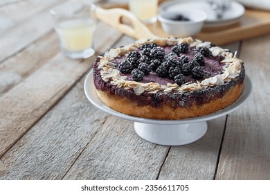 Fruit cake with fresh blackberries and almond flakes served whole on cake stand front view on wooden table - Shutterstock ID 2356611705