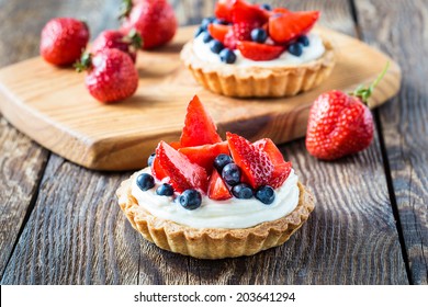 Fruit dessert tarts with cream, strawberry and blueberry on wooden table - Powered by Shutterstock