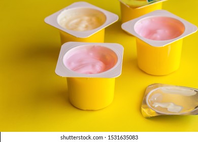 Fruit flavoured yogurt in yellow plastic cups on bright yellow background with silver foil lid - Yoghurt cup background with selective focus