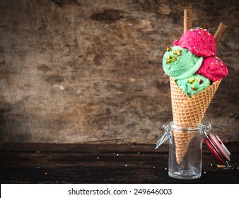 Fruit ice cream in cone on wooden background with blank space 
