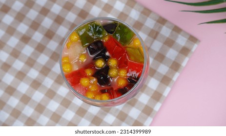 fruit ice with various kinds of fruit such as melon and watermelon there is also black jelly red yellow clear white glass checkered tablecloth photo taken from above on a pink background object - Powered by Shutterstock