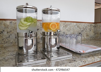 Fruit Infused Flavored Water In Beverage Dispenser With Fresh Oranges And Apples.
