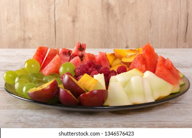 Fruit Mix. Peach, Grapes, Apple, Watermelon, Melon, Raspberry, Plum. Pieces Of Fruit On A Plate Lie On A White Wooden Background. Copy Space, Space For Text.