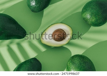 Fruit pattern made of avocado with palm leaves shadow on pastel green background. Minimal nature food layout. Tropical summer fruit concept. Original background image with a play of light and shadow.