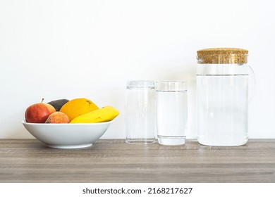 A fruit plate stands with water glasses and a water carafe on a wooden table