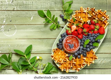 
					Fruit platter with berries and freshly baked waffles, strawberries, blueberries, green wooden background, rustic, summer fruits, jam, sauce, fruit, sweet, juicy, summer, breakfast, snack, copy space