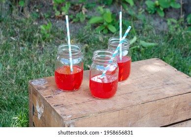 Fruit Punch In Glass Jars With Paper Straws, Sitting On A Wooden Box Outside. 