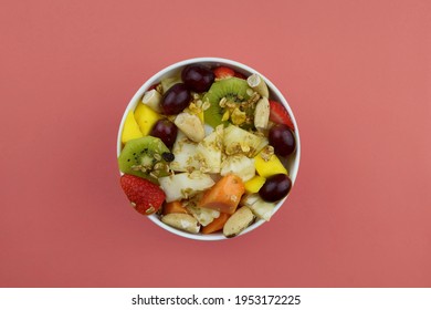 Fruit salad with chestnuts and granola in a bowl. Multicolored ripe fruits. Pineapple, mango, grape, strawberry, papaya, melon, banana and kiwi. Pink background - Shutterstock ID 1953172225