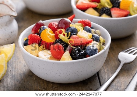 Fruit salad with fresh berries, bananas and apples in small bowls with mint and citrus dressing