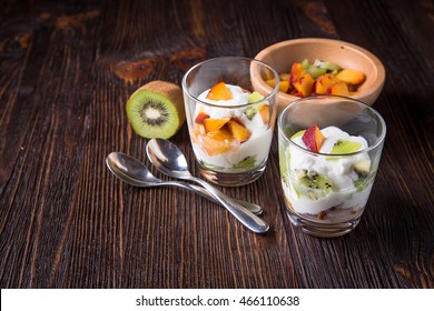 Fruit salad in glass goblets of kiwi and peaches with yogurt on dark table