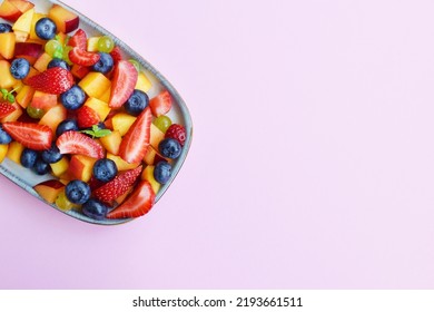 Fruit salad in a rectangular plate on a pink background. Sliced strawberries, peaches and blueberries with mint leaves. - Shutterstock ID 2193661511
